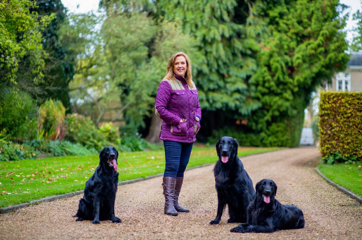 Jenny Campbell with 3 Flatcoated Retrivers on gravel driveway
